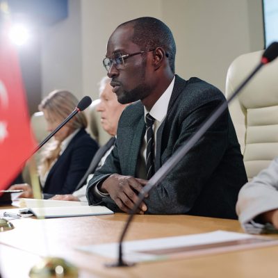 African American businessman giving an interview while sitting at table with his colleagues at conference